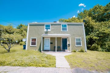 New Haven apartment for rent - A house with a grey siding and a white door is surrounded by greenery.