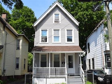 New Haven apartment for rent - A two-story house with a white porch and a black car parked in front.