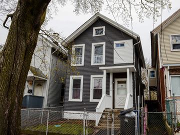 New Haven apartment for rent - A house with a gray siding and white trim is surrounded by a chain link fence.