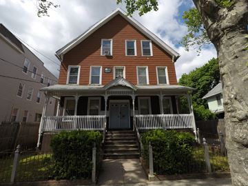 New Haven apartment for rent - A brown house with a white fence and a green bush in front.