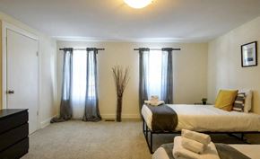 Manayunk triplex for rent - A bedroom with a bed, dresser, and window with curtains.