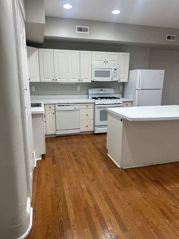 Manayunk triplex for rent - A kitchen with white cabinets and appliances.