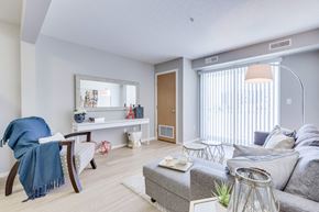 Kelowna apartment for rent - A living room with a grey couch, a white coffee table, a blue chair, and a mirror on the wall.