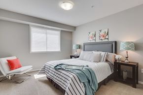Kelowna apartment for rent - A bedroom with a bed, chair, and nightstand.