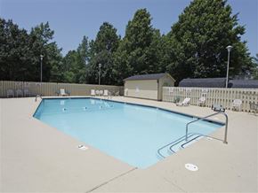 Fayetteville apartment for rent - a swimming pool with chairs around it and trees in the background