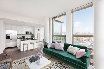 Hoboken apartment for rent - A modern living room with a green couch and a kitchen area in the background.