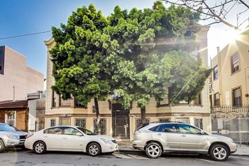 San Francisco apartment for rent - Two cars parked in front of a building with a large tree in the background.