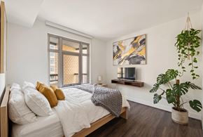 Washington apartment for rent - bedroom with bed, small tv, plants in the corner, dark wood flooring and window