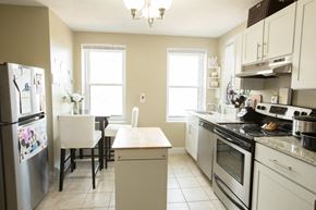 Boston apartment for rent - a white kitchen with stainless steel appliances and a dining room table