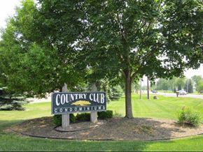 Grand Blanc condo for rent - A sign that says Country Club Condominiums is in front of a tree.