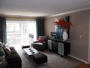 Simi Valley apartment for rent - A living room with a black couch, a grey armchair, a black coffee table, and a black cabinet with a vase of red flowers on top.