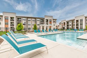 Fort Worth apartment for rent - A swimming pool surrounded by lounge chairs in front of apartment buildings.