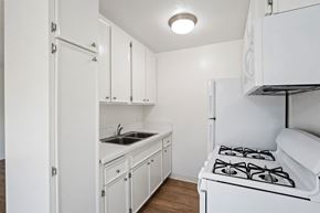 Studio City apartment for rent - Clean, compact kitchen at the Excelsior apartment community in Studio City featuring white cabinetry, a double-basin sink, gas stove, refrigerator, built-in microwave, and wood-style flooring.