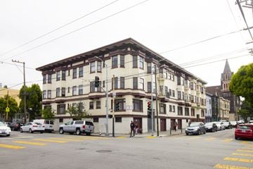 San Francisco apartment for rent - A street view of a multi-story building with cars parked in front.