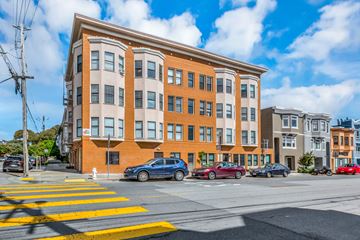 San Francisco apartment for rent - A street view of a multi-story building with cars parked in front.