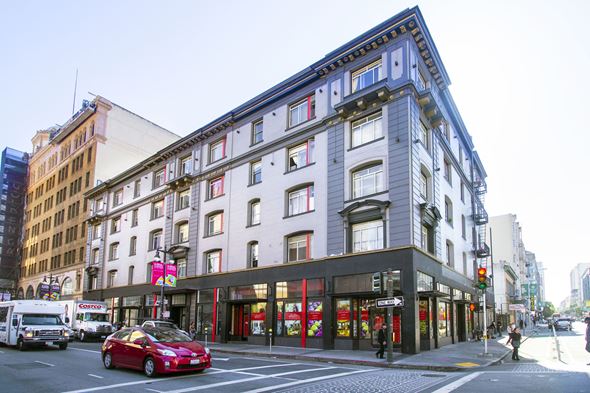 San Francisco apartment for rent - A red car is driving down a street past a building with a black awning.
