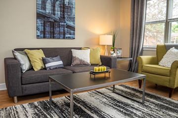 St. Louis apartment for rent - A living room with a grey couch, a coffee table, a yellow chair, and a large painting on the wall.