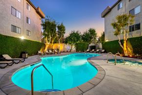 Lake Balboa apartment for rent - A glowing, swimming pool at the Parkview Apartments in Lake Balboa. The turquoise water is lit from within, with lounge chairs on the surrounding deck and warmly lit trees against a twilight sky.