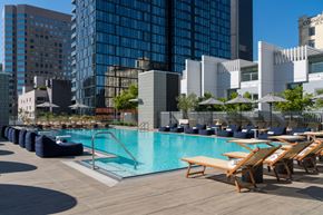 Los Angeles apartment for rent - A pool surrounded by lounge chairs and umbrellas with buildings in the background.
