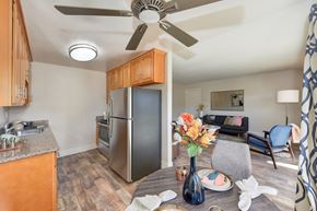Hayward apartment for rent - A kitchen with a refrigerator, a ceiling fan, and a dining table with a vase of flowers on it.