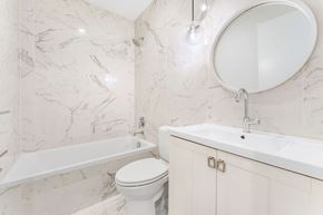 Jersey City apartment for rent - A white toilet sits next to a sink in a marble bathroom.