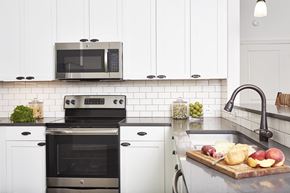 Amityville apartment for rent - A modern kitchen with a black oven and microwave, white cabinets, and a cutting board with fruits and cheese on the counter.