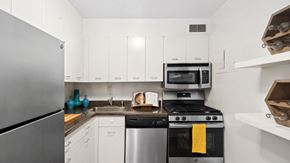 Chicago apartment for rent - A small kitchen with white cabinets and stainless steel appliances, including a refrigerator, dishwasher, stove, and microwave. There is a cookbook open on a stand near the stove and a yellow towel ha