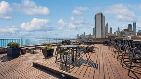 Chicago apartment for rent - Looking across the rooftop deck with Lake Michigan and the Chicago skyline in the background. Various deck furniture is set throughout the deck.