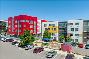 Lakewood apartment for rent - A parking lot with cars and a red building in the background.