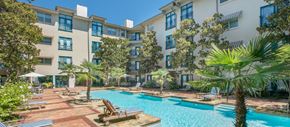 Dallas apartment for rent - a large swimming pool with chairs and trees in front of an apartment building