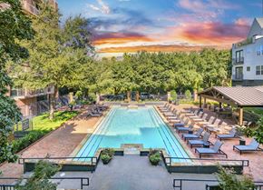 Dallas apartment for rent - A large outdoor swimming pool surrounded by lounge chairs and trees.
