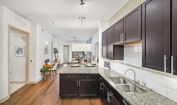 Dallas apartment for rent - a kitchen with granite counter tops and dark cabinets and a living room