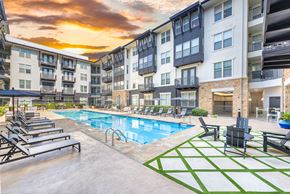 Austin apartment for rent - A sunset view of a pool area with lounge chairs and a green and white patterned rug.