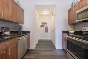 Burlington apartment for rent - a kitchen with wooden cabinets and black counter tops and a long hallway