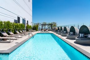 Los Angeles apartment for rent - A long rectangular pool with a blue tinted water surrounded by sun loungers and umbrellas.