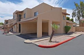 Mesa apartment for rent - an empty parking lot in front of a tan building with a palm tree