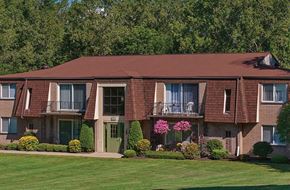 Orchard Park apartment for rent - A large building with a green door and windows surrounded by bushes and trees.