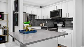 Chicago apartment for rent - Looking across the kitchen island at a residence kitchen at Eleven Thirty. The cabinets are white with a black, subway tile backsplash. The stainless oven and microwave or in the middle with the refri