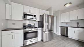 Chicago apartment for rent - Looking closely at the stainless steel appliances in a kitchen at Grand Plaza. The oven and microwave are on the left, with the refrigerator in the middle. The dishwasher is off to the right. The cabi