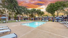 Dallas apartment for rent - A sunset view of a pool area with lounge chairs and umbrellas.