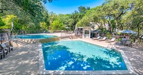 Austin apartment for rent - A large swimming pool surrounded by trees and lounge chairs.