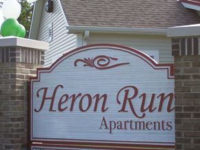 Smyrna apartment for rent - A sign for Heron Run Apartments is displayed in front of a house.
