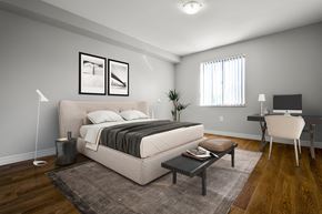Kitchener apartment for rent - A bedroom with a large bed, a desk with a chair, and a rug on the floor.