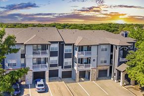 Mckinney apartment for rent - A sunset view of a multi-story apartment building with cars parked in the driveway.