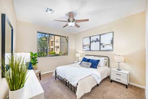 Gilbert apartment for rent - A bedroom with a large bed, a ceiling fan, and a window with a view of a building outside.