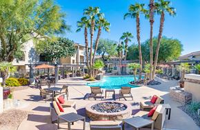 Gilbert apartment for rent - A pool surrounded by palm trees and patio furniture.