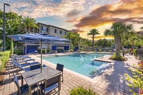 Gainesville apartment for rent - a swimming pool with tables and chairs and a building in the background