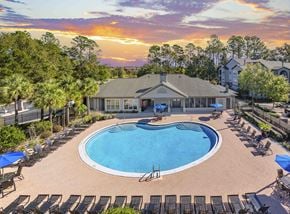 Tallahassee apartment for rent - A sunset view of a pool area with lounge chairs and umbrellas.