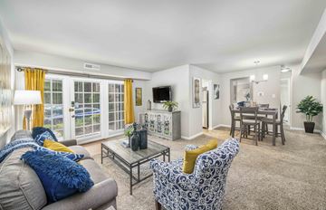Fredericksburg apartment for rent - A living room with a grey couch, a blue and white patterned armchair, a glass coffee table, and a dining area with a table and chairs.