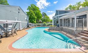 Memphis apartment for rent - A swimming pool surrounded by a stone wall and a patio area with chairs.